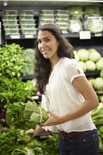 Hispanic woman holding lettuce in grocery store
