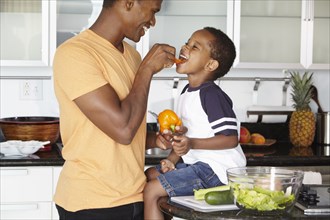 African American father and son eating vegetables in kitchen