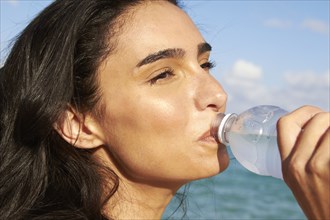 Hispanic woman drinking water bottle on beach
