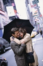 Couple huddled under umbrella on city street