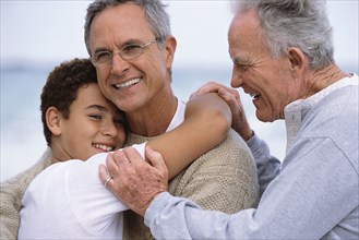 Three generations of Caucasian men hugging on beach