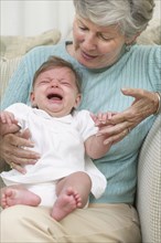 Senior woman with crying granddaughter on sofa