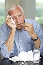 Senior man wiping his nose and taking medicine