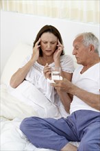 Senior man giving wife painkillers in bed