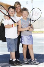 Mother and children holding tennis rackets outdoors