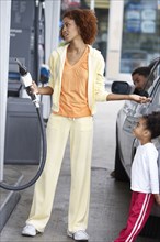 Black mother using pump at gas station