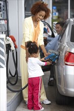 Black mother teaching daughter to pump gas