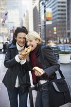 Women eating pretzel on city street