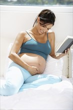 Pregnant Hispanic woman reading in bed