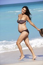 Pregnant Hispanic woman walking on beach
