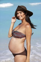 Pregnant Hispanic woman smiling on beach