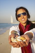 Middle Eastern woman holding seashells on beach