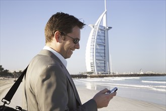Caucasian businessman using cell phone on beach
