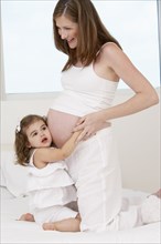 Caucasian girl hugging mother's pregnant belly
