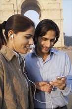 Indian couple listening to headphones by monument
