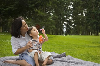 Boy blowing bubbles in park with mother