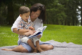 Boy reading story book in park with mother