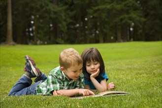 Brother and sister reading story book in park