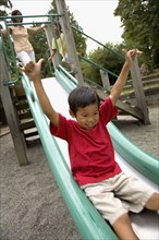 Asian boy sliding down slide on playground