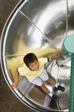 Asian boy sliding down circular slide