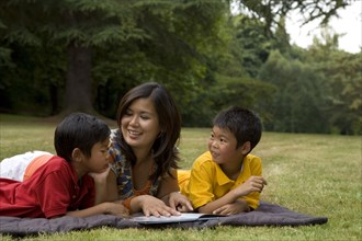 Asian mother reading book to sons in park
