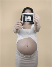 Pregnant Chinese woman holding out sonogram image