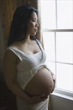 Pregnant Asian woman standing near window