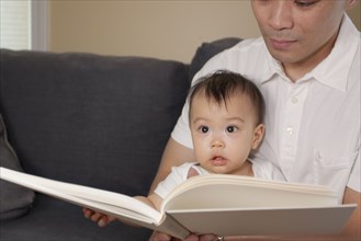 Chinese father and baby reading book on sofa