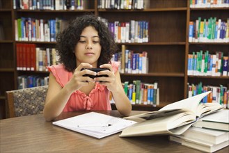 Mixed race girl text messaging on cell phone in library