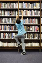 Boy reaching for book on library shelf