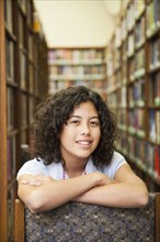 Mixed race girl leaning on chair in library