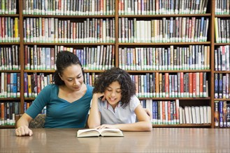 Mother helping daughter read book in library