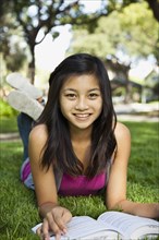 Asian girl laying in grass reading book