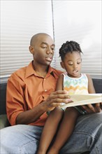 Black father reading book to daughter