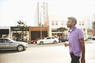 African American man with coffee cup walking on sidewalk