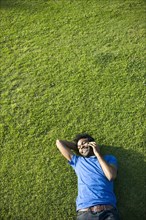 African American man using cell phone laying on grass