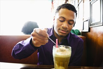 Mixed race man enjoying milkshake in diner booth