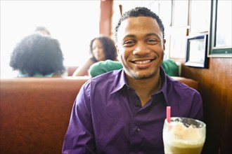 Smiling mixed race man with milkshake in diner booth