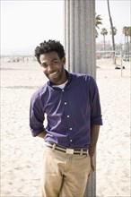 African American man leaning on pole at beach