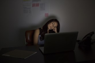 Businesswoman sleeping at desk at night