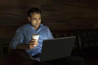 Businessman using laptop on sofa at night