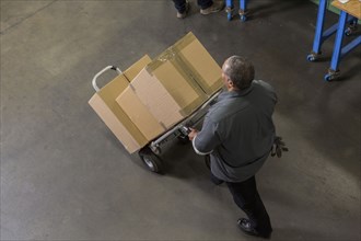 Worker carting boxes on hand truck in warehouse