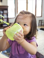 Mixed race girl drinking from sippy cup in kitchen