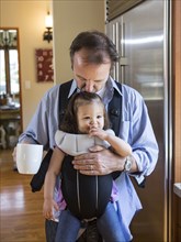 Father holding daughter in sling in kitchen