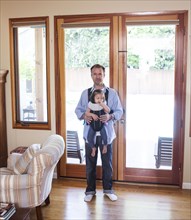 Father holding daughter in sling in living room