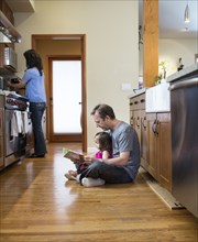Father reading to daughter in kitchen