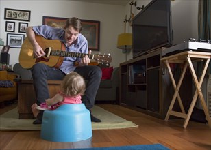 Caucasian father playing guitar for daughter