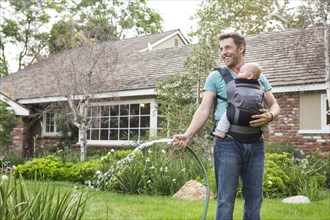 Caucasian father holding baby and watering plants