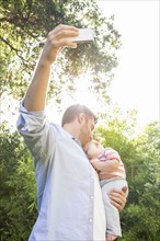Caucasian father taking cell phone picture with baby in backyard