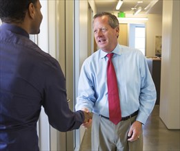 Businessmen shaking hands in office hallway